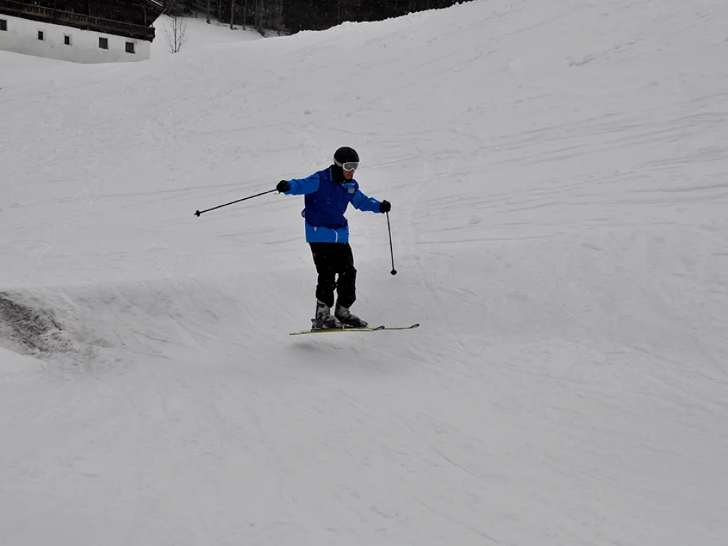 Skifahrer in blauer Jacke auf dem Hang vor einem Gebäude.